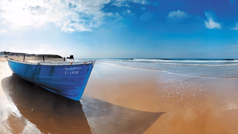 Traditional blue fishing boat resting on the sandy beach of Agadir, Morocco under a clear blue sky